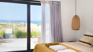 A bedroom with a bed, a view of the outdoors, and a hanging light fixture. - Hidden Hill Villas (Naxos)