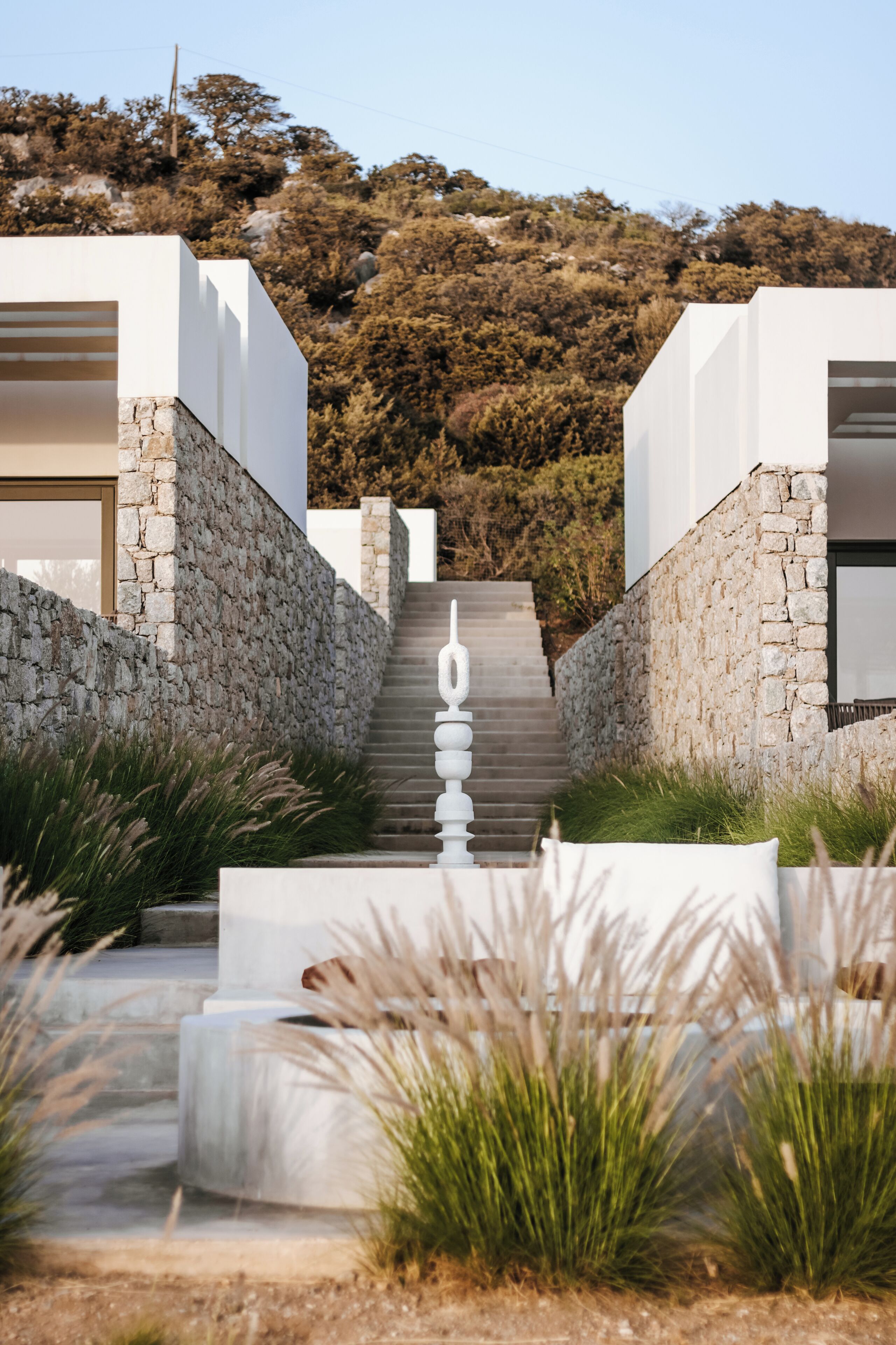 A modern building with a stone facade, a staircase leading to a door, and a view of a hillside.