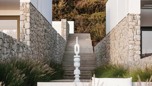 A modern building with a stone facade, a staircase leading to a door, and a view of a hillside. - Hidden Hill Villas (Naxos)