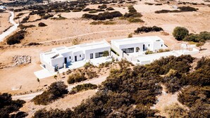 A modern white building with a flat roof, surrounded by sparse vegetation and a clear view of the sea in the background. - Hidden Hill Villas (Naxos)