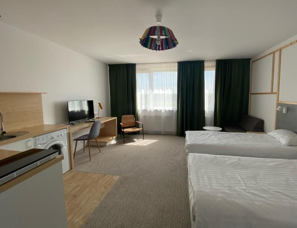 A hotel room with a bed, a desk, a chair, a television, and a washing machine.