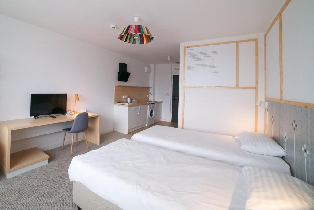 Ein Hotelzimmer mit zwei Betten, einem Schreibtisch, einem Fernseher und einer Küchenzeile.