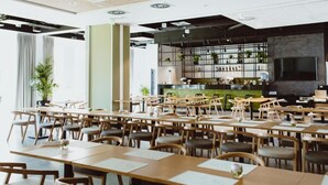 A spacious restaurant with multiple wooden tables and chairs, a bar area with shelves of bottles, and a large TV screen. - Arche Hotel Poloneza (Warsaw)