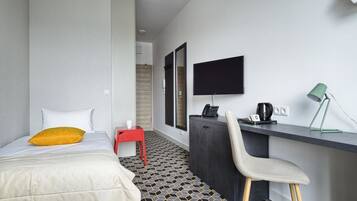 Quarto de hotel com cama, escrivaninha, cadeira, televisão e luminária.