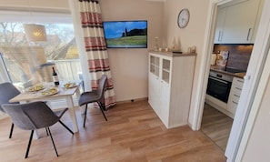 Un espace de vie compact comprenant un coin repas, un téléviseur, une cuisine et une vue par la fenêtre.
