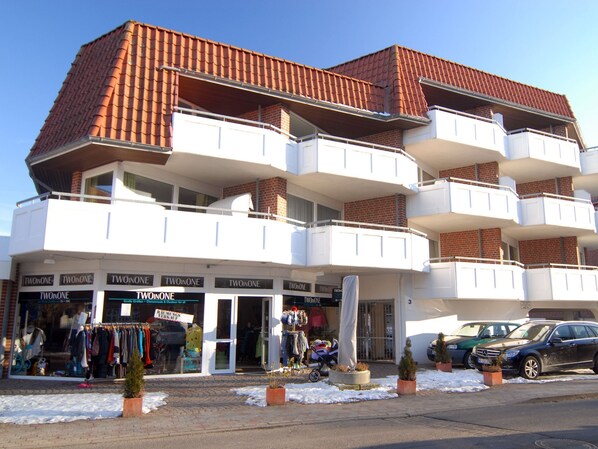 Un edificio de varios pisos con balcones, locales comerciales y coches estacionados.