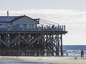 A pier with a building on top, a sandy beach, and the ocean in the background.