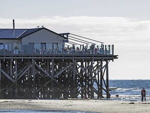 Un molo con un edificio sulla sommità, una spiaggia sabbiosa e l'oceano sullo sfondo.