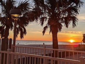 A sunset view from a beachside promenade with palm trees and a wooden fence.