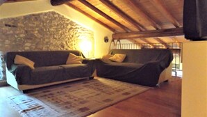 A cozy attic room with a stone wall, wooden beams, a sofa, and a television. - Casa Canevini Garda (Garda)