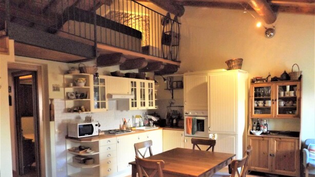 A compact kitchen with white cabinets, a wooden dining table, and chairs. - Casa Canevini Garda (Garda)