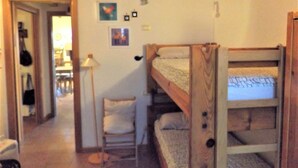 A room with bunk beds, a chair, and a lamp. There are pictures on the wall and a door leading to another room. - Casa Canevini Garda (Garda)