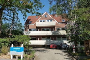 Ein zweistöckiges Wohngebäude mit rotem Ziegeldach und einem Balkon im oberen Geschoss. Ein Schild weist auf 'utlande apartments' hin.