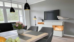 Ein modernes Wohnzimmer mit Esstisch, Stühlen, einem Fernseher und einem großen Fenster.