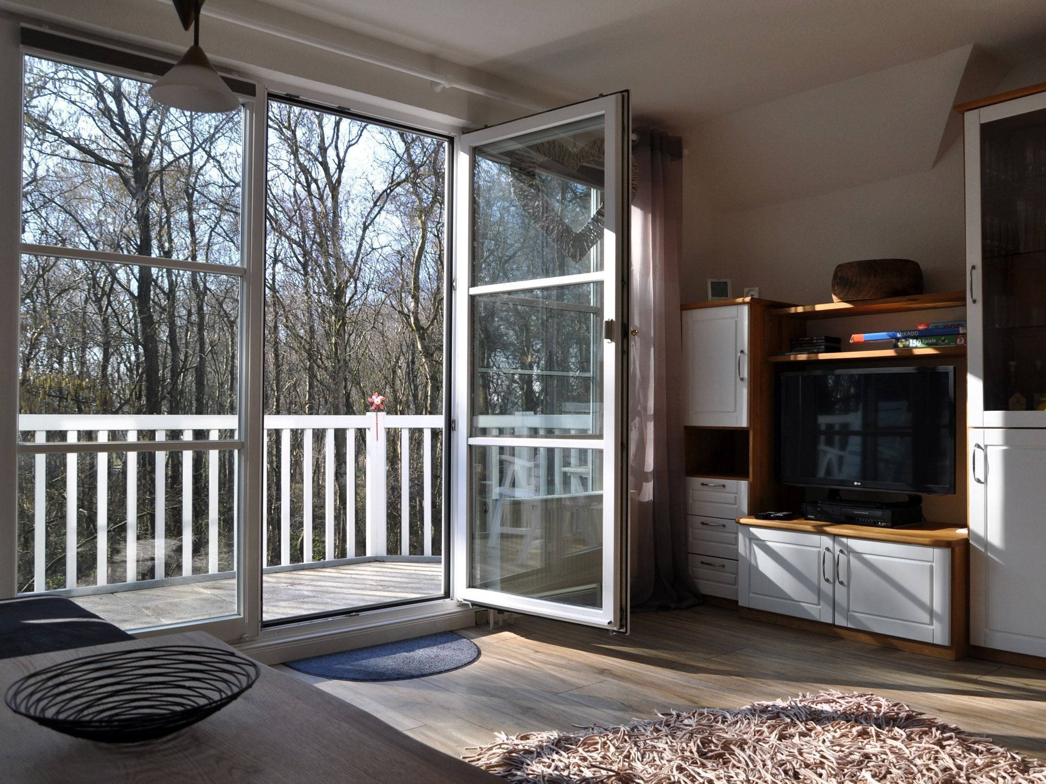 A modern kitchen with a large sliding glass door leading to a deck, wooden cabinets, and a built-in TV.