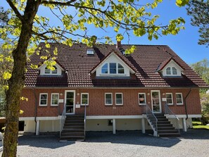 A two-story brick building with a red-tiled roof, multiple windows, and a gravel driveway. - House In The Bathroom 74 - House In The Bathroom 74 Whg 05 (Sankt Peter-Ording)