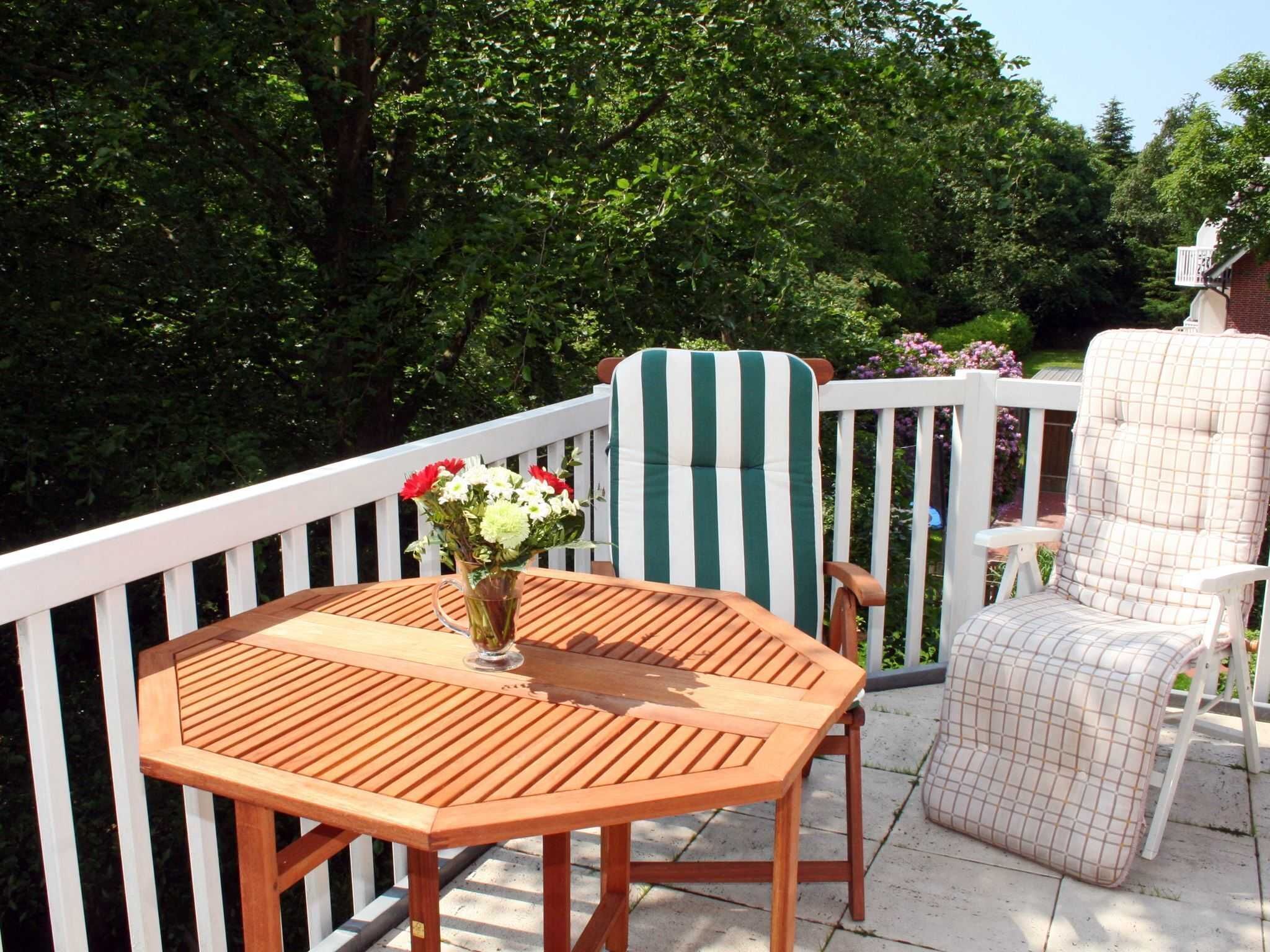 An outdoor patio with a wooden table and chairs, surrounded by a white railing.