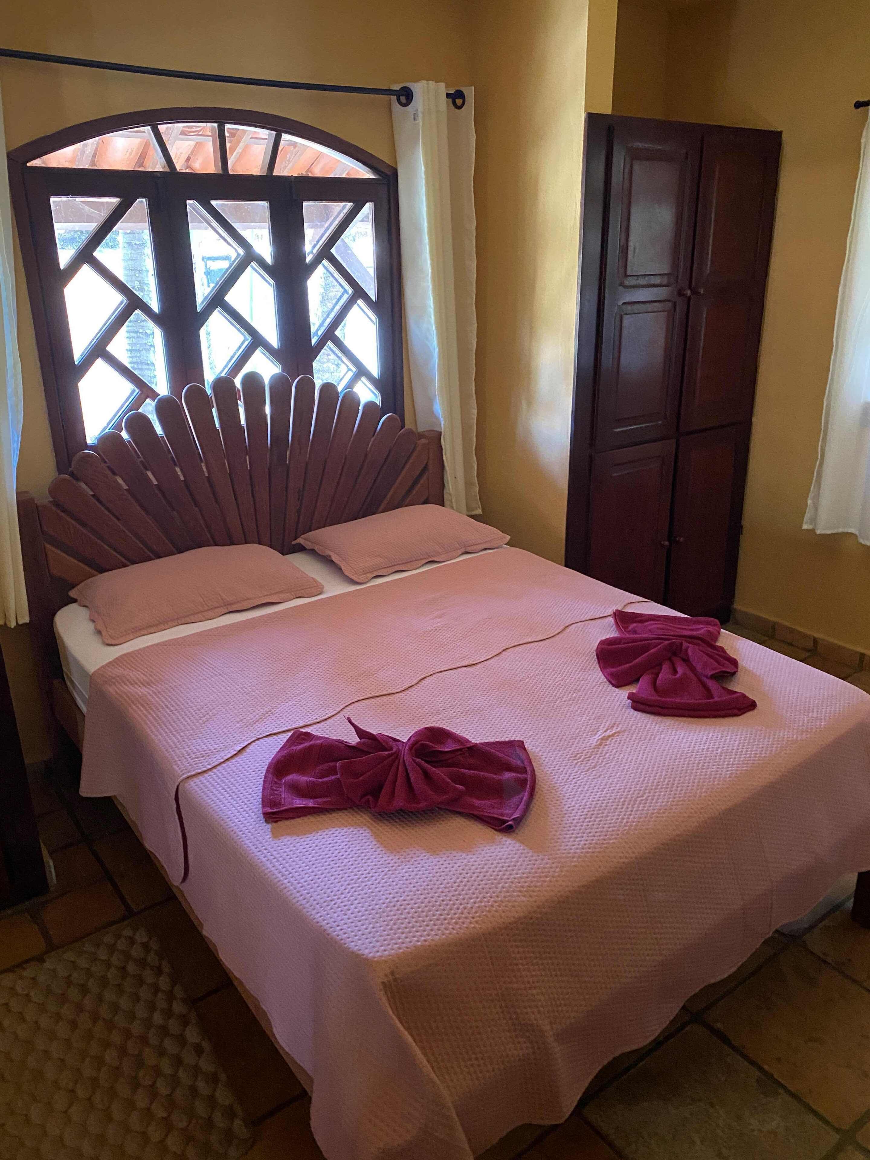 Una cama con un cabecero original, un armario y una ventana con cortinas.
