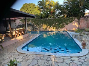 A swimming pool with stone tiles, a wooden bench, and a stone wall with greenery. - Taverna do Paraíso (Paulista)