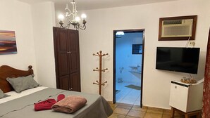 A bedroom with a bed, a TV, a coat rack, and a door leading to a bathroom. - Taverna do Paraíso (Paulista)
