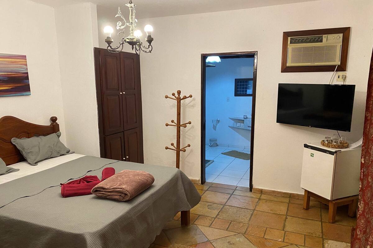 Quarto com cama, televisão, cabideiro e porta que dá para um banheiro.