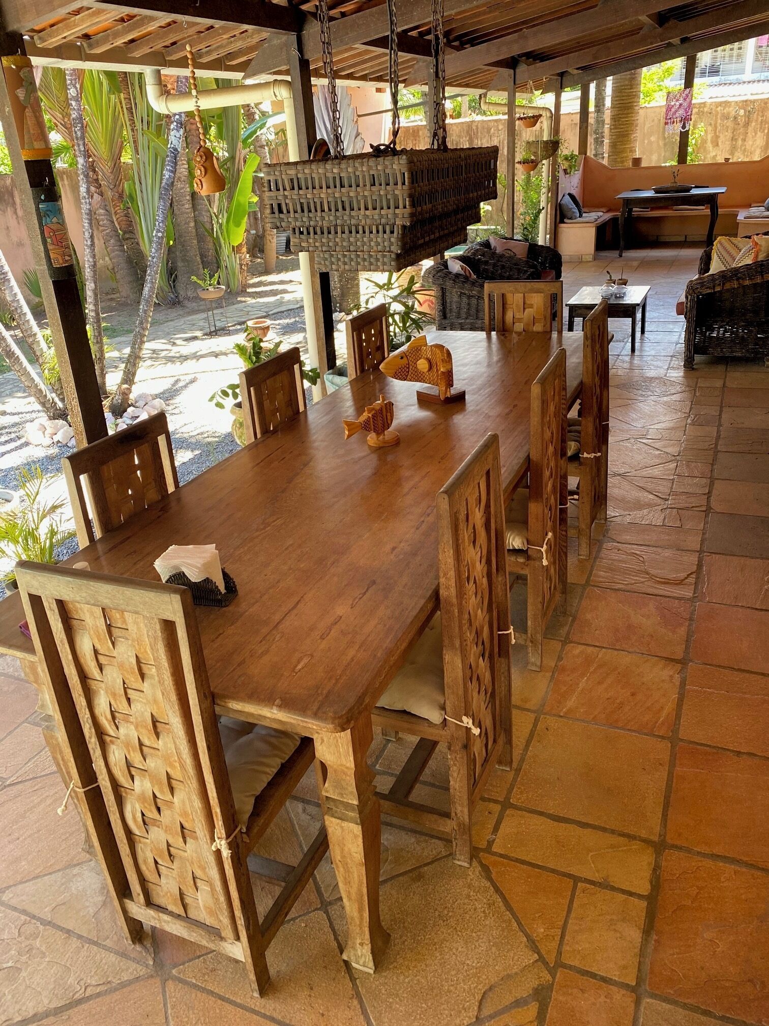 Una mesa de madera con sillas, cestas colgantes y vistas al exterior.