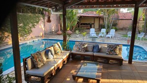 A covered outdoor seating area with a pool, lounge chairs, and a patio table. - Taverna do Paraíso (Paulista)