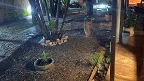 A covered outdoor area with a stone pathway, potted plants, and a thatched structure. - Taverna do Paraíso (Paulista)