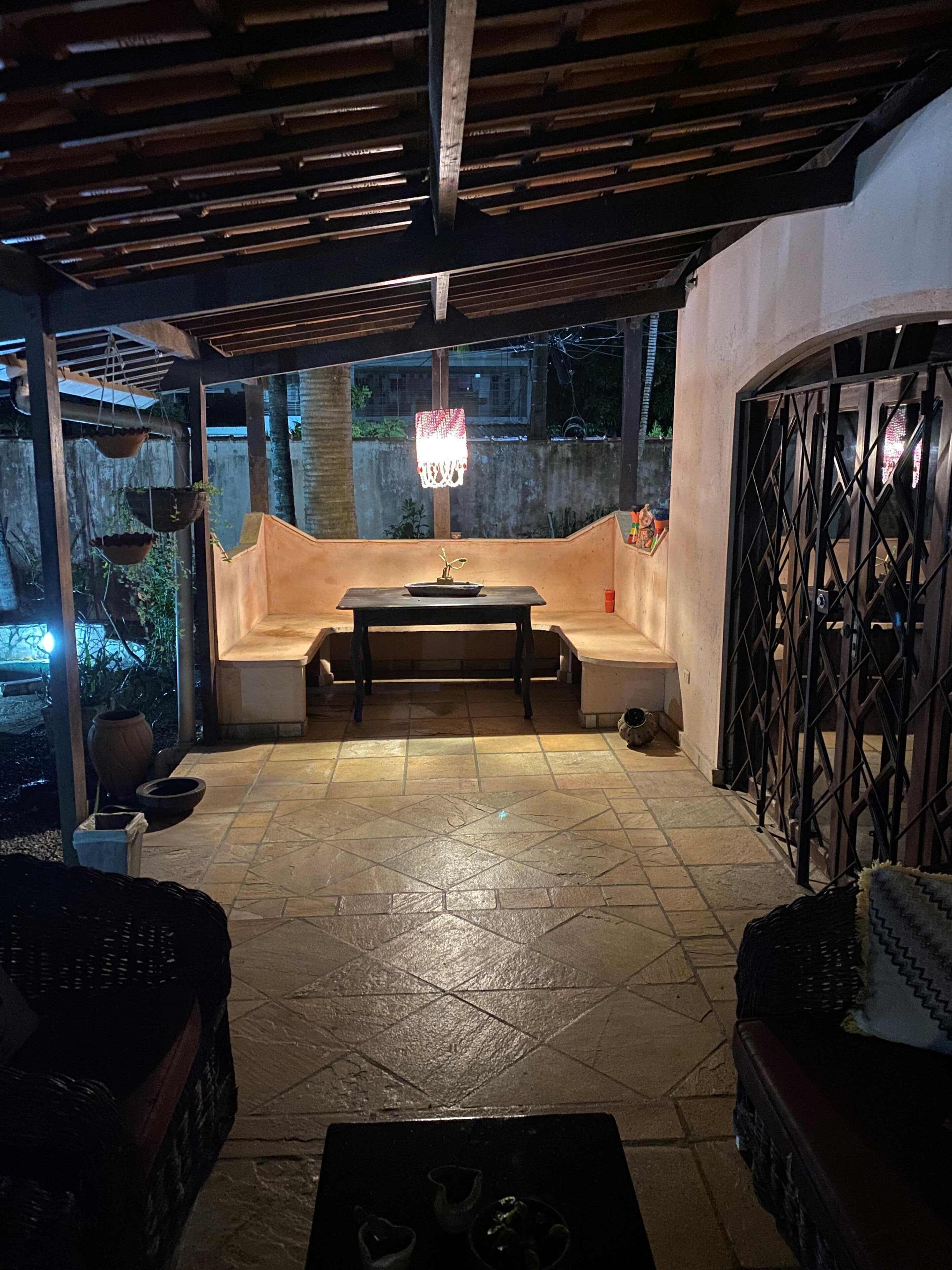 An outdoor patio with a table and benches, a hanging light fixture, and a metal gate.
