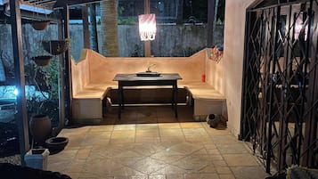 Un patio al aire libre con una mesa, bancos, una lámpara colgante y una reja de metal.