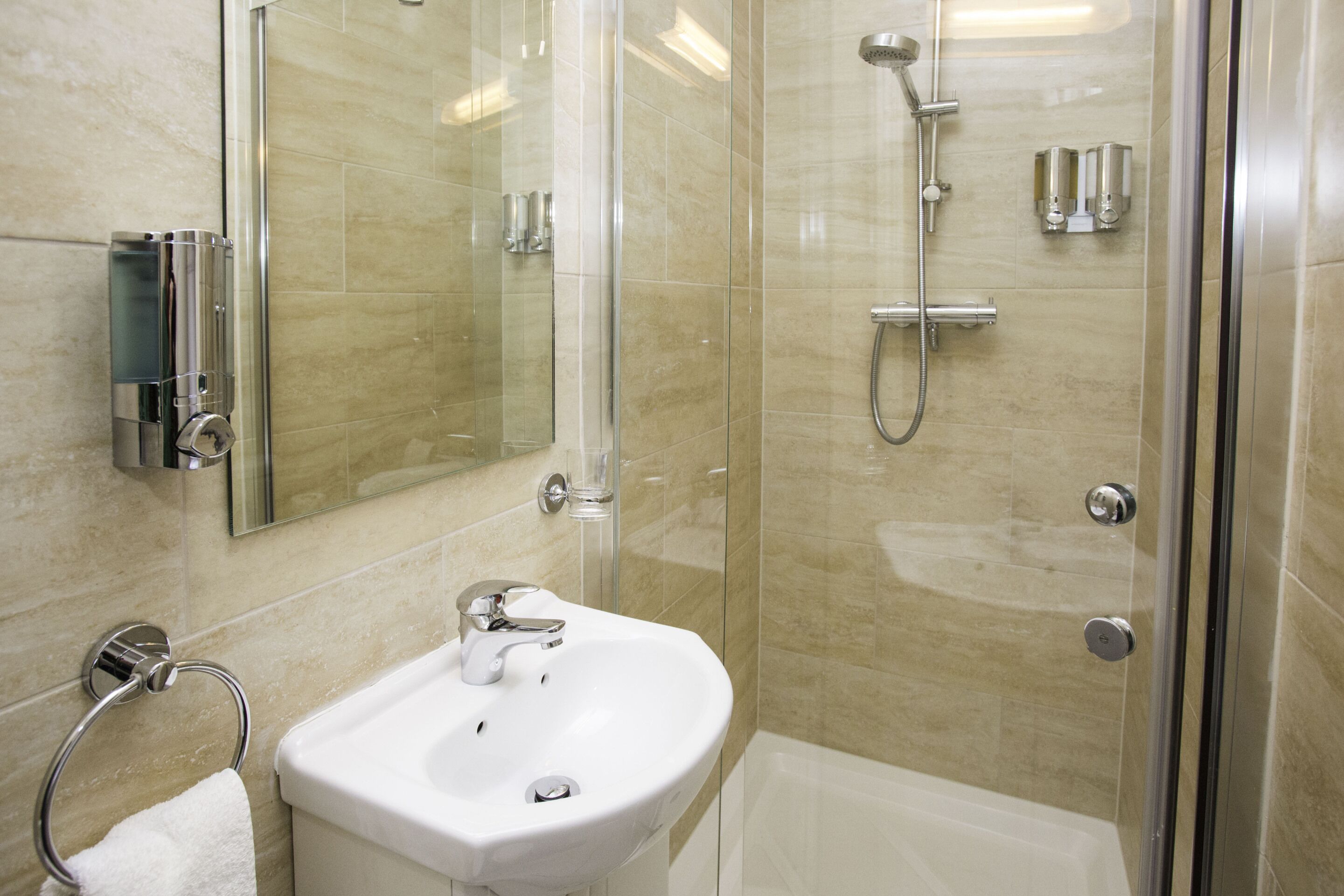 Een moderne badkamer met een douche met glazen wand, een witte wastafel en een spiegel.