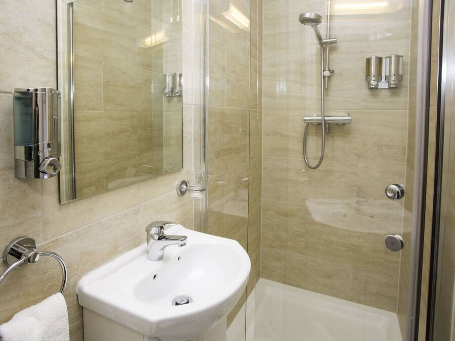 Een moderne badkamer met een douche met glazen wand, een witte wastafel en een spiegel.