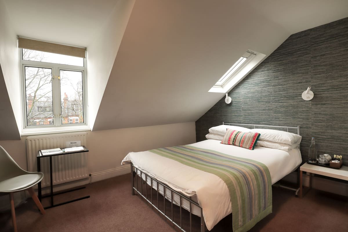 A bedroom with a bed, a radiator, a window, a desk, and a nightstand.