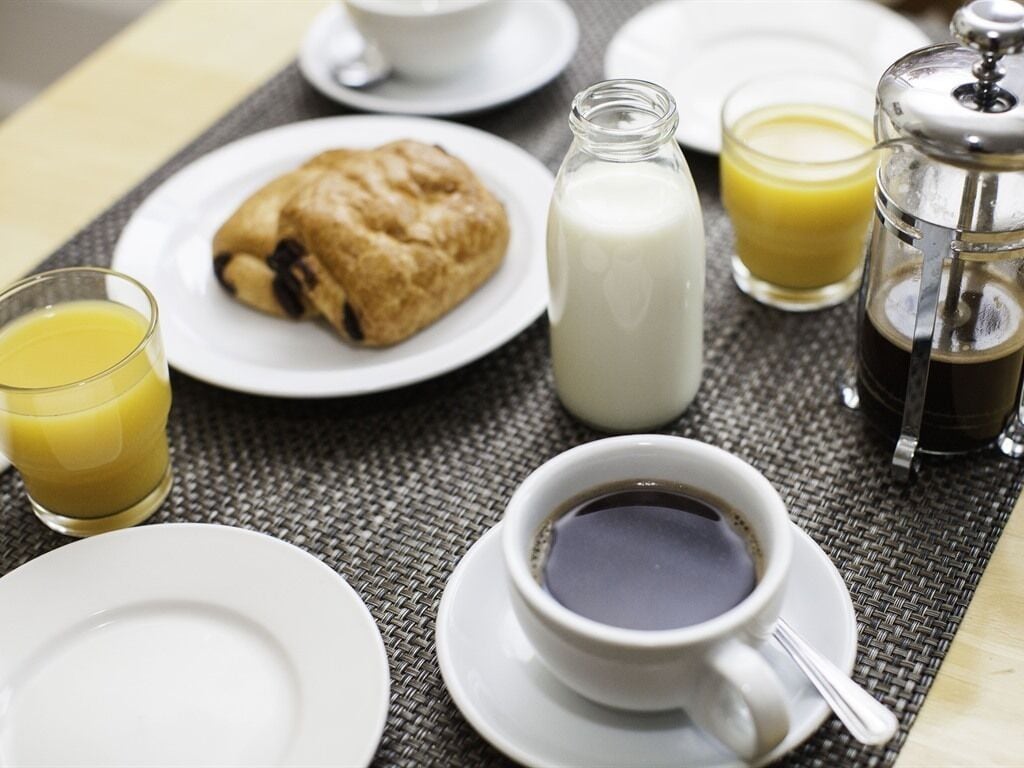 A breakfast setting with a croissant, milk, orange juice, coffee, and a French press.