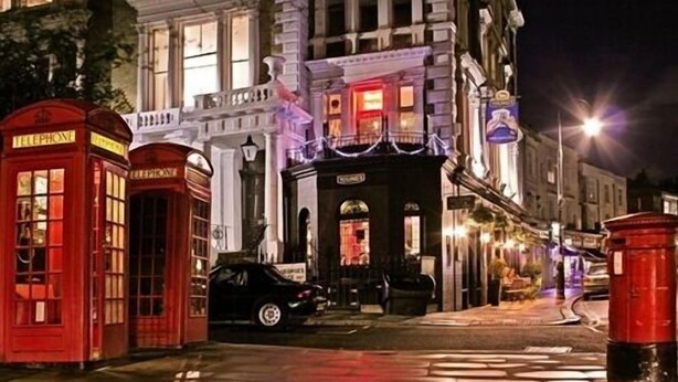 A street scene with a red telephone booth, a black car parked in front of a building with a large archway, and a red post box. - Primrose Guest House (London)