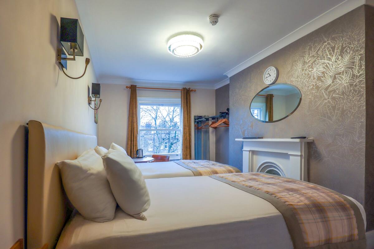 Habitación de hotel con dos camas, un espejo, un reloj y una chimenea.