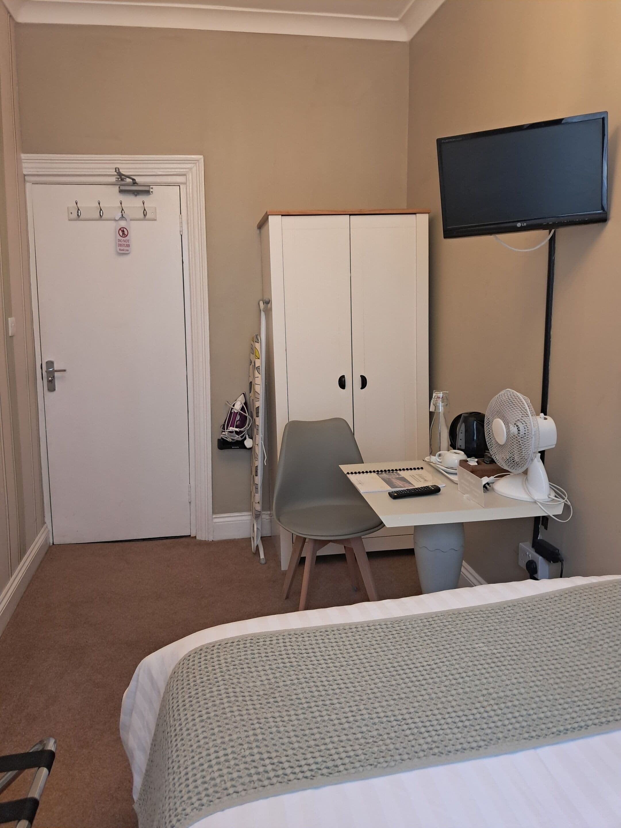 Une chambre d’hôtel comprenant un lit, un bureau avec une chaise, un téléviseur fixé au mur et une armoire.