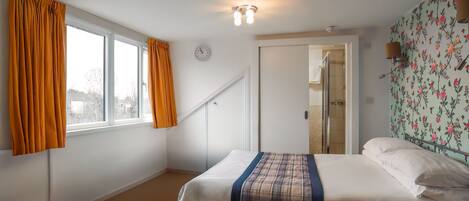 Un dormitorio con cama, ventana con cortinas, un reloj y papel tapiz floral.