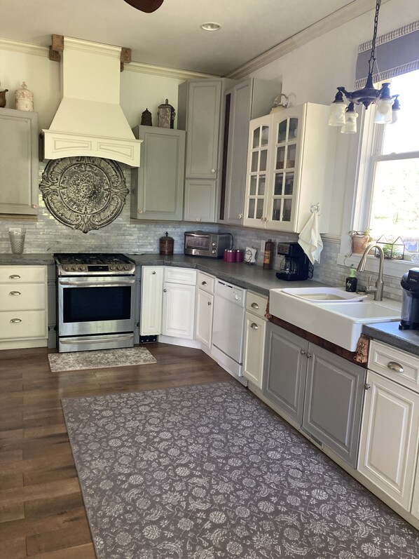 A kitchen with white cabinets, a stainless steel stove, a built-in oven, a sink, and a patterned rug.