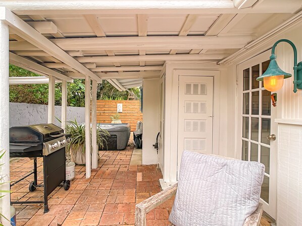 A covered patio with a grill, hot tub, and outdoor seating area.