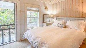 Un dormitorio con una cama grande, ventilador de techo, ventana con persianas y vistas a zonas verdes.