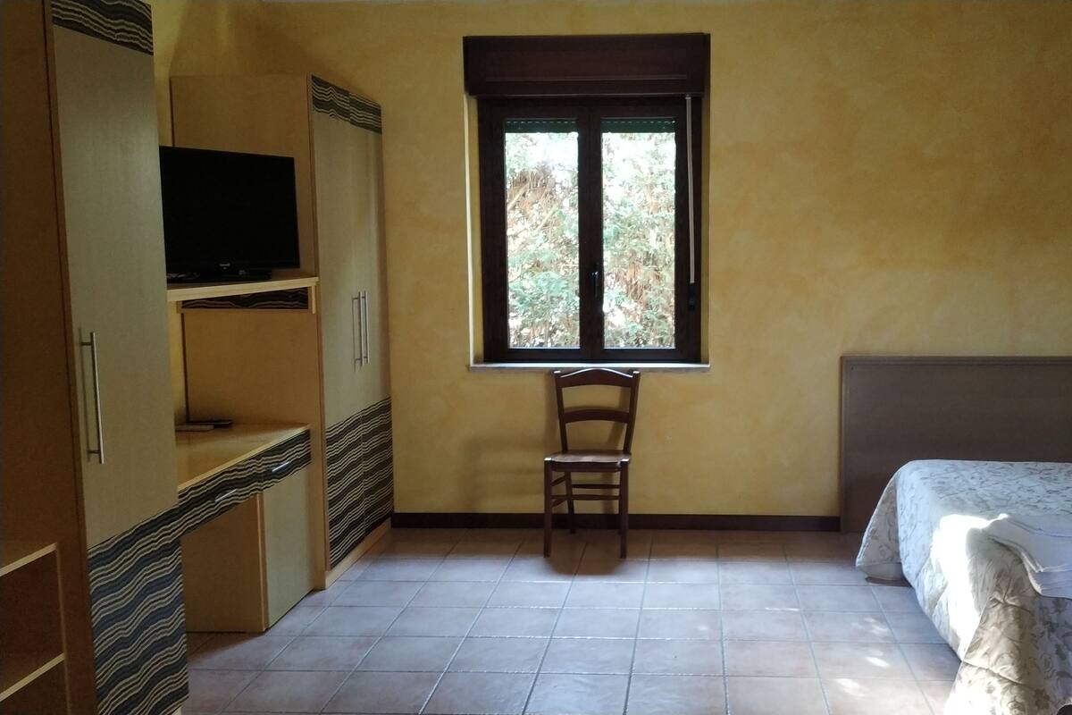 A bedroom with a bed, a chair, a TV, and a window.