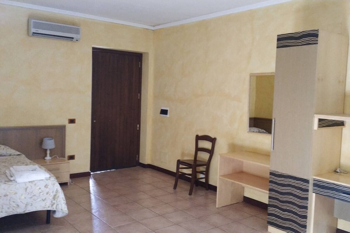 A hotel room with a bed, a desk, a chair, a TV, and a wardrobe.