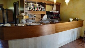A bar area with a wooden counter, shelves with various bottles, glasses, and a coffee machine. - Amarcord (Spezzano Albanese)
