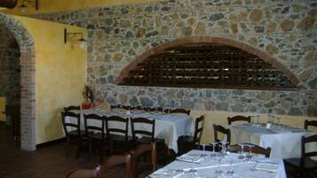 A restaurant with stone walls, multiple tables set with wine glasses, and a wine rack above the tables.