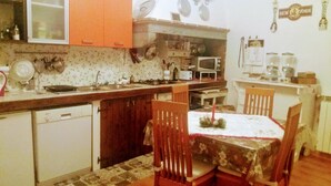 A kitchen with wooden cabinets, a dining table with chairs, a microwave, and a refrigerator. - La Maison del Corso B&B (Pisa)