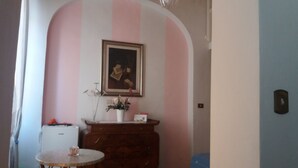 A room with a pink and white striped wall, a framed picture, a small table with a vase, and a wooden cabinet. - La Maison del Corso B&B (Pisa)