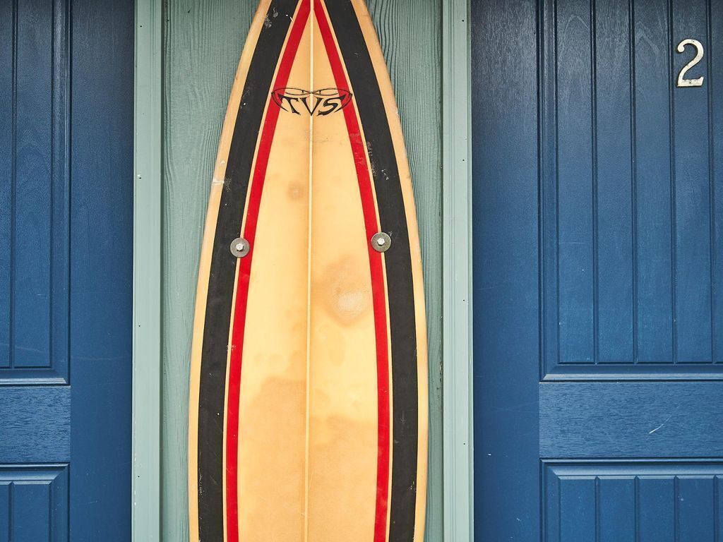 Un aldabilla con forma de tabla de surf y un logo, fijada a una puerta azul con el número 2.