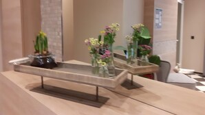 A reception desk with a glass display case containing flowers and a potted plant. - Hotel Marco Polo (Münster)