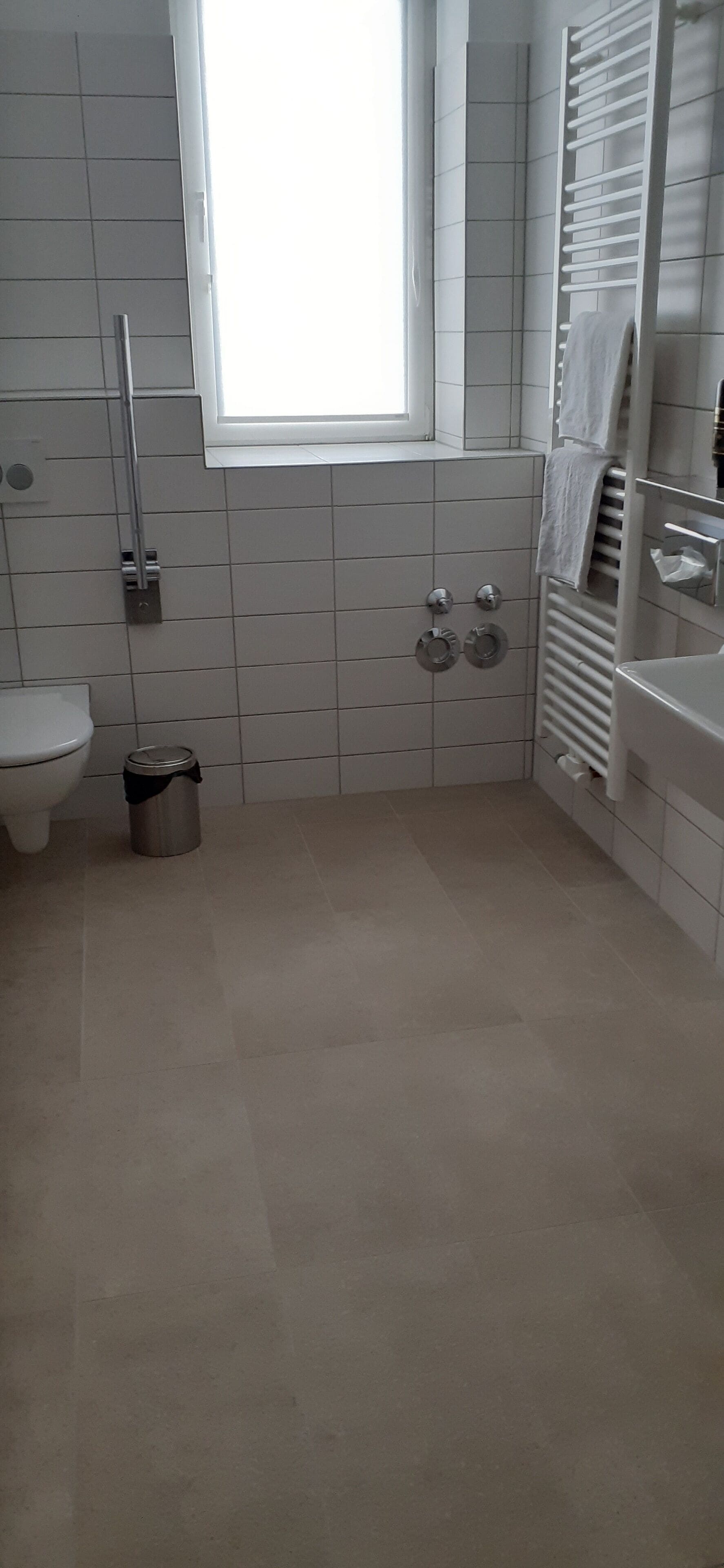 A bathroom with a toilet, a bidet, a towel rack, and a window.